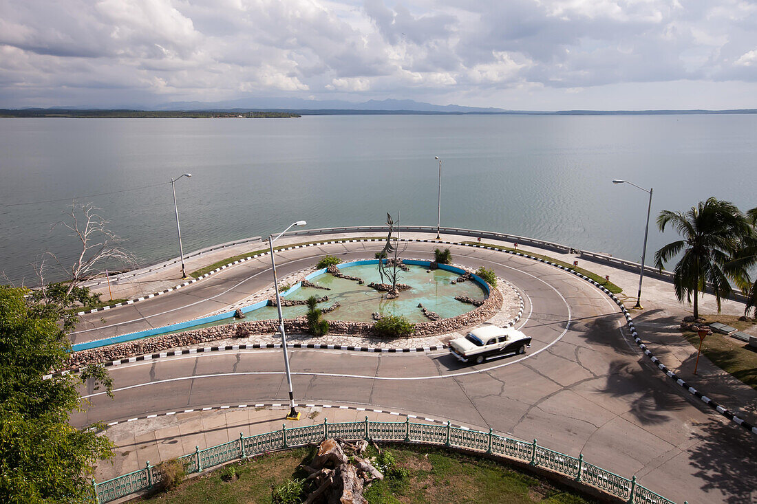 Entlang der Uferpromenade in Cienfuegos fährt ein amerikanischer Oldtimer durch einen Kreisverkehr,Cienfuegos,Kuba