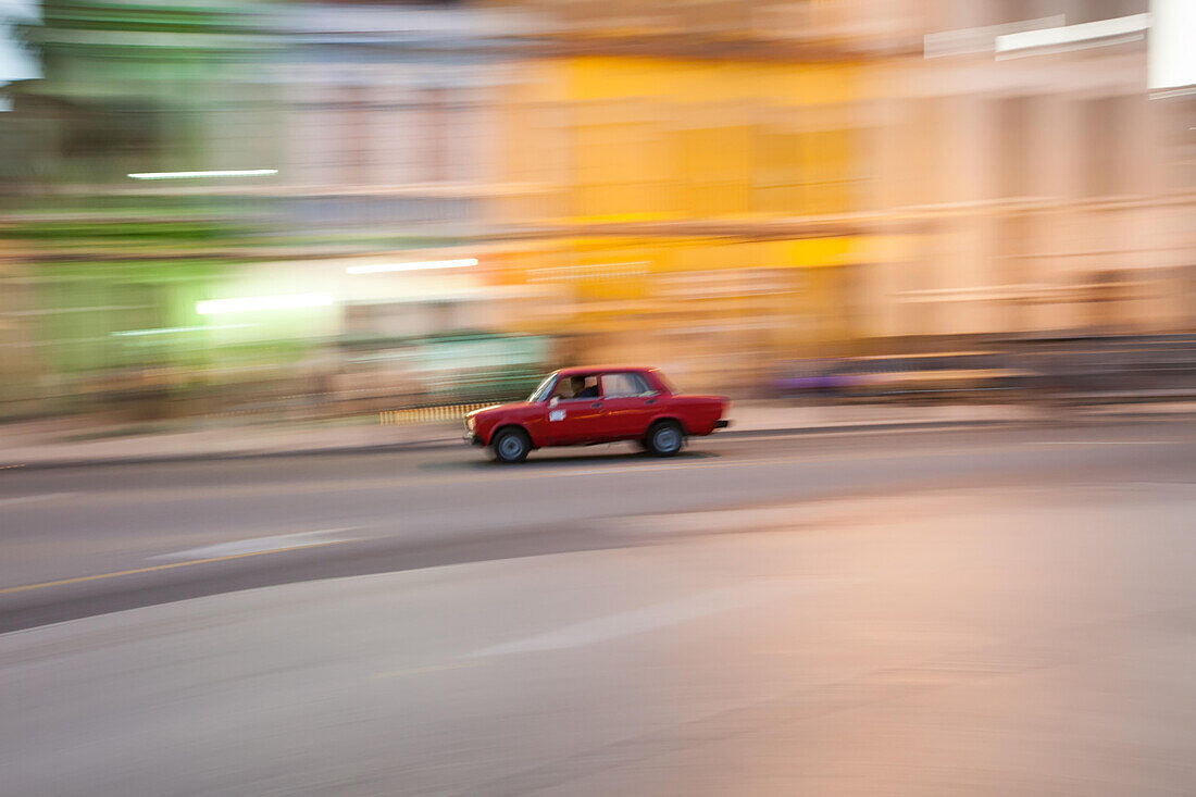 An old,red car speeds down the street in downtown Havana.,Havana,Cuba