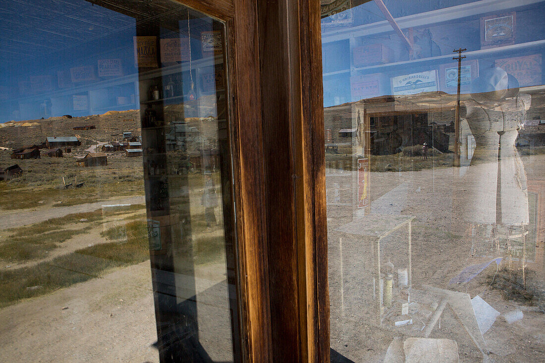 Das Innere eines verlassenen Gemischtwarenladens und die umgebende Landschaft, die sich in einem Schaufenster spiegelt,Bodie State Historic Park,Bridgeport,Kalifornien