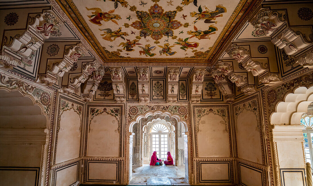 Frauen sitzen in einer Fensternische einer bemalten Halle in Ahhichatragarh Fort, Nagaur, Rajasthan, Indien