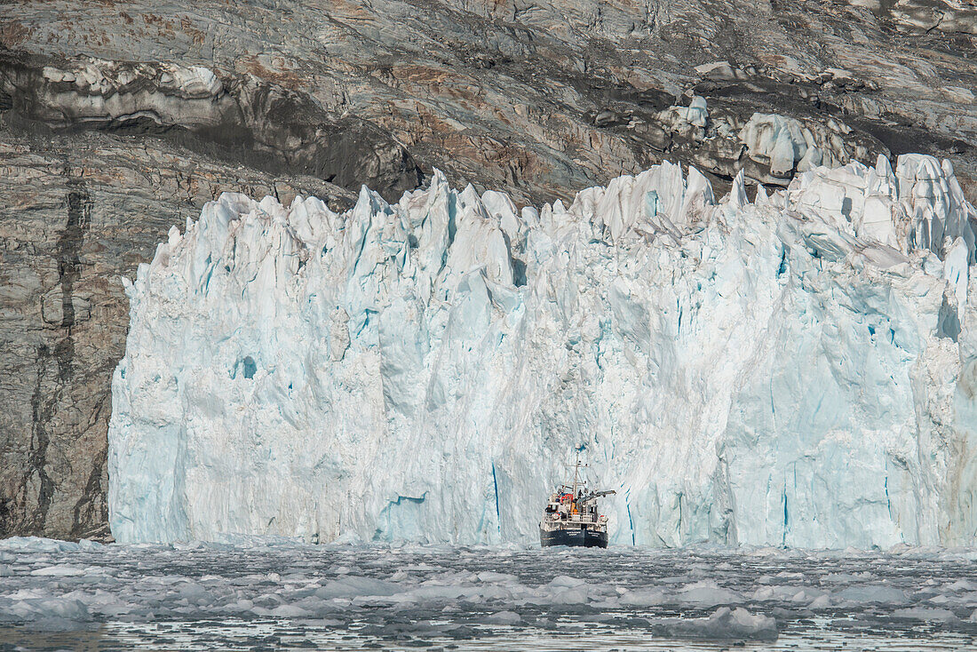 Schiff vor der eisigen Wand eines Gezeitengletschers an der Küste der Insel Südgeorgien mit dem kabbeligen Meereiswasser des Südlichen Ozeans, Südgeorgien, Antarktis