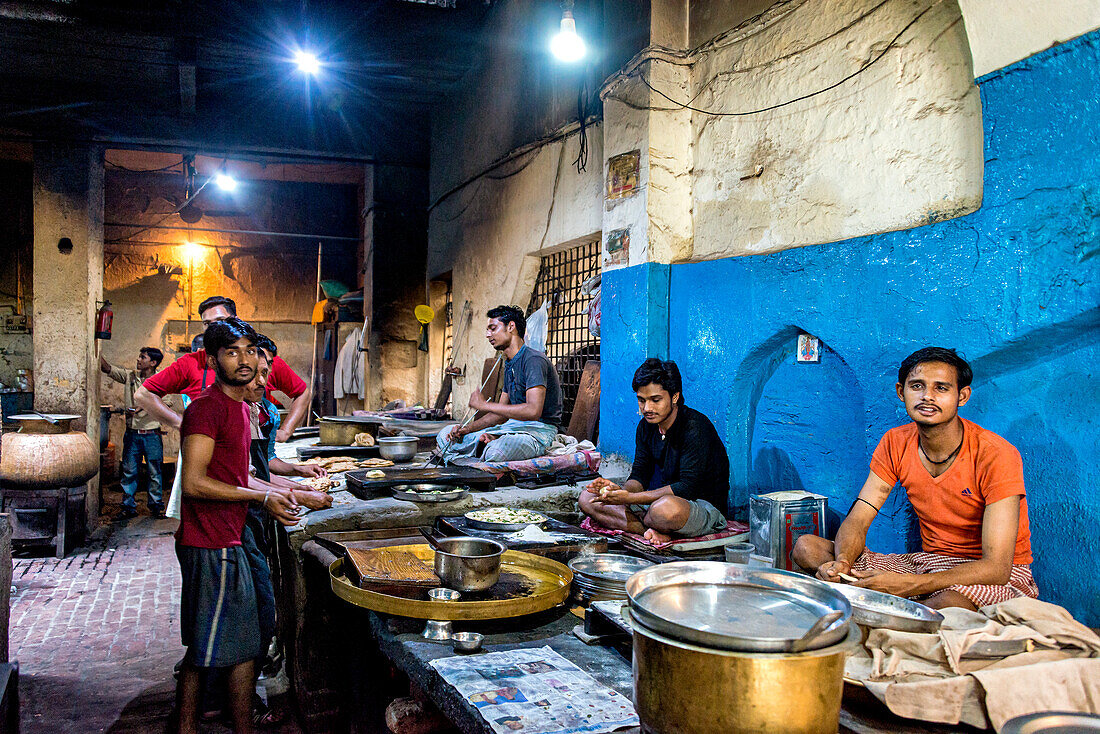 Junge Männer arbeiten in einer Großküche und bereiten unter Beleuchtung Lebensmittel zu in Indien, Amritsar, Punjab, Indien