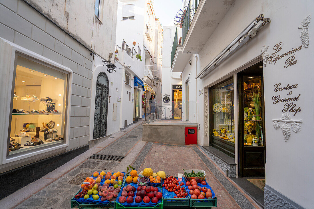 Modegeschäfte und ein Stand mit frischem Gemüse und Obst in einer engen Straße in Capri, Capri, Neapel, Italien