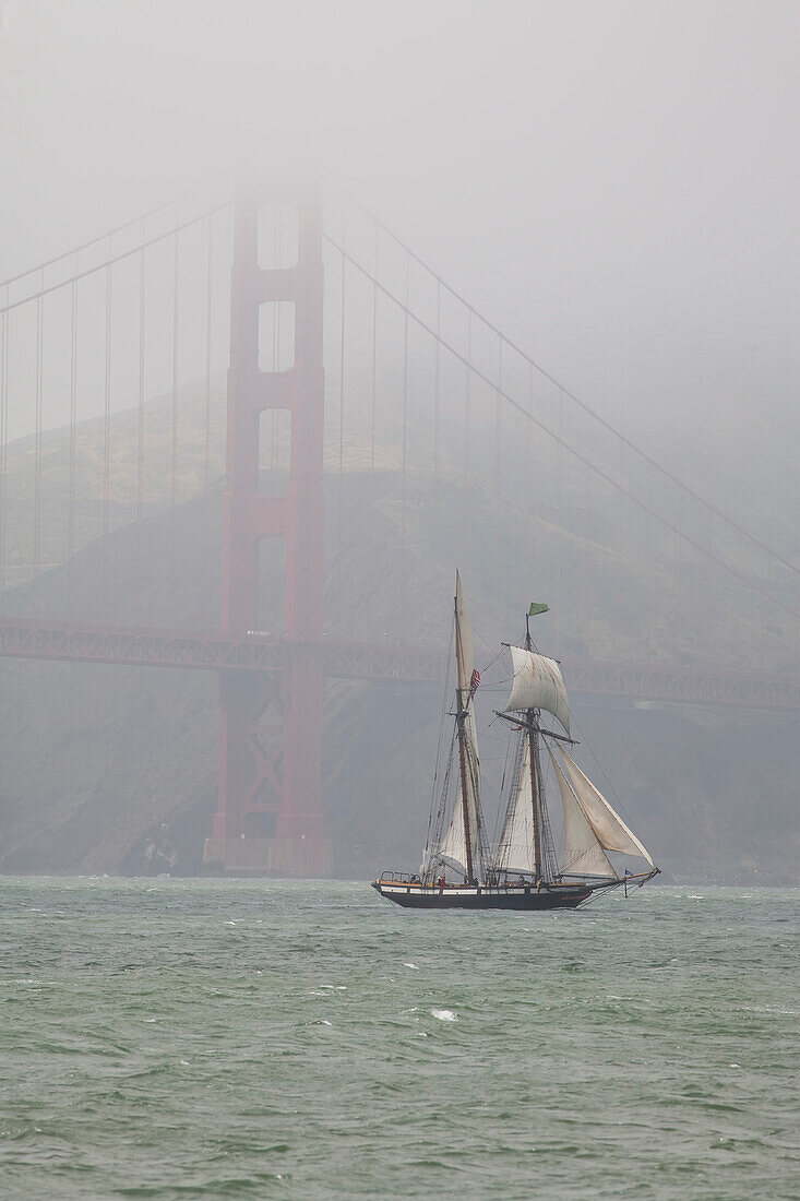 A two masted schooner sails under the Golden Gate Bridge.,San Francisco,California.