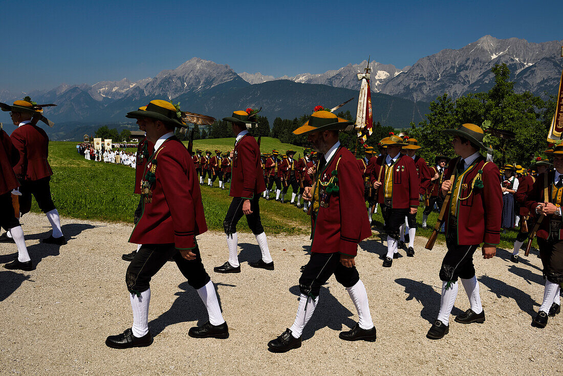 Der Festzug zum Herz-Jesu-Fest zieht in eine große Wiese ein, die vom Karwendelgebirge überragt wird.