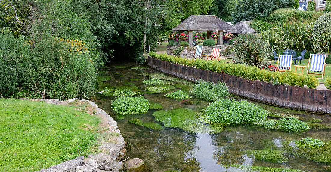 Sitzgelegenheiten am Flussufer in Gärten entlang des Flusses Coln, Bibury, Gloucestershire, England