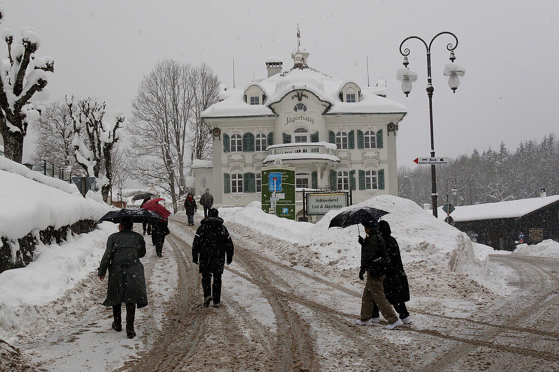 Touristen tragen Regenschirme, um während eines Wintersturms in Füssen, Deutschland, schneebedeckte Straßen hinaufzugehen,Füssen,Deutschland