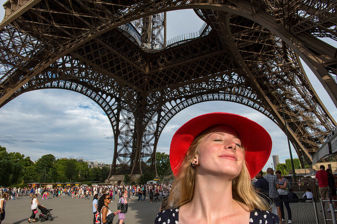 Junge Frau mit rotem Hut steht unter dem Eiffelturm und sonnt sich im Sonnenlicht in Paris,Frankreich,Paris,Frankreich