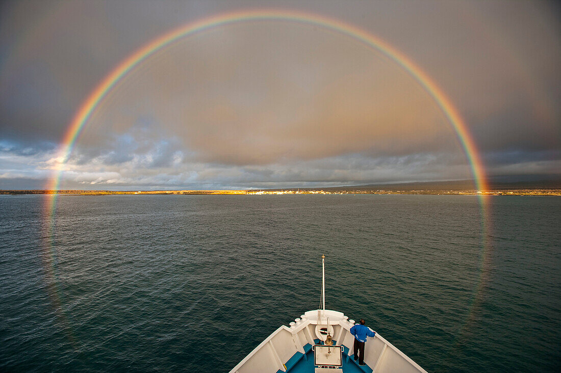 Ein runder Regenbogen umgibt den Bug eines kleinen Kreuzfahrtschiffes auf den Galapagos-Inseln, Santa Cruz Island, Galapagos-Inseln, Ecuador