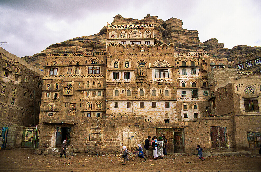 Kinder spielen und Erwachsene unterhalten sich vor einem jemenitischen Dorfgebäude, Wadi Dhar, Jemen