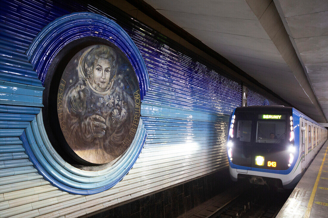 Der Zug fährt auf den Gleisen an einem Bild des Kosmonauten Konstantin Ziolkowski, der ersten Frau im Weltraum, an den dekorierten Wänden der Kosmonawtlar-Station der Taschkenter Metro in Usbekistan vorbei, Taschkent, Usbekistan