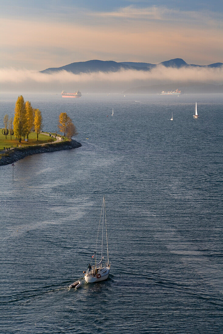 Segeln auf die English Bay hinaus, wo Schiffe im Nebel vor Anker liegen und die Uferpromenade einen Blick auf die Bucht und die Coast Mountains bietet, Vancouver, British Columbia, Kanada