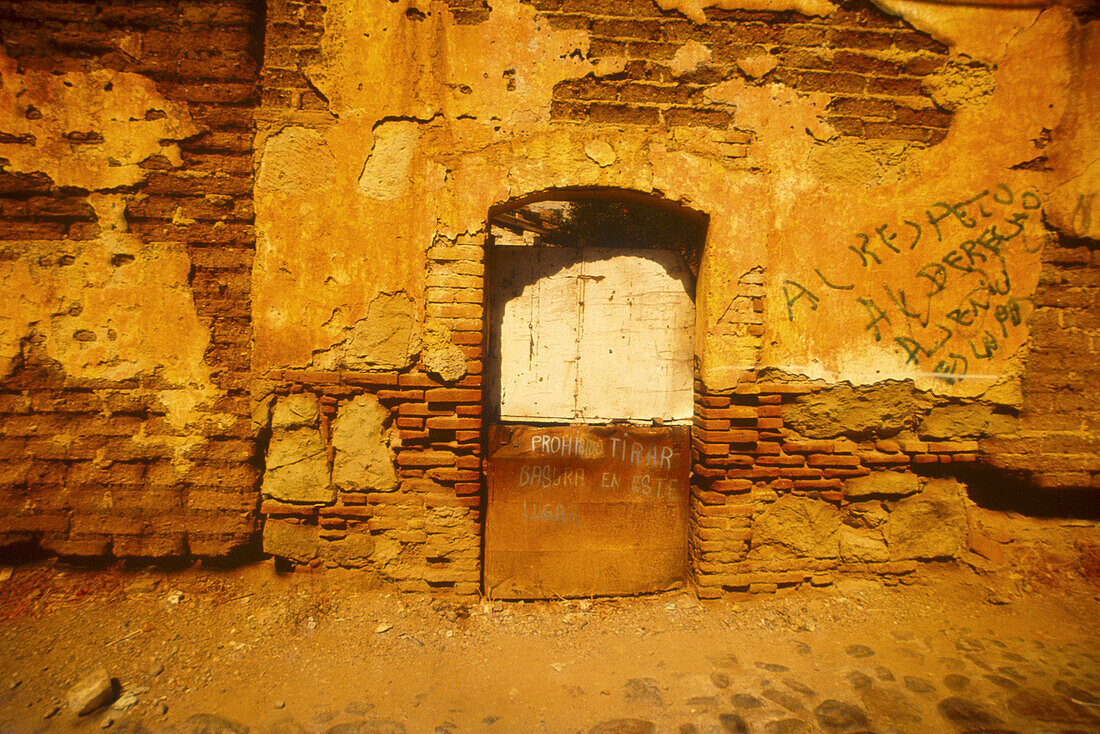 Verfallende Steinmauer mit Tür und Graffiti, Oaxaca, Mexiko