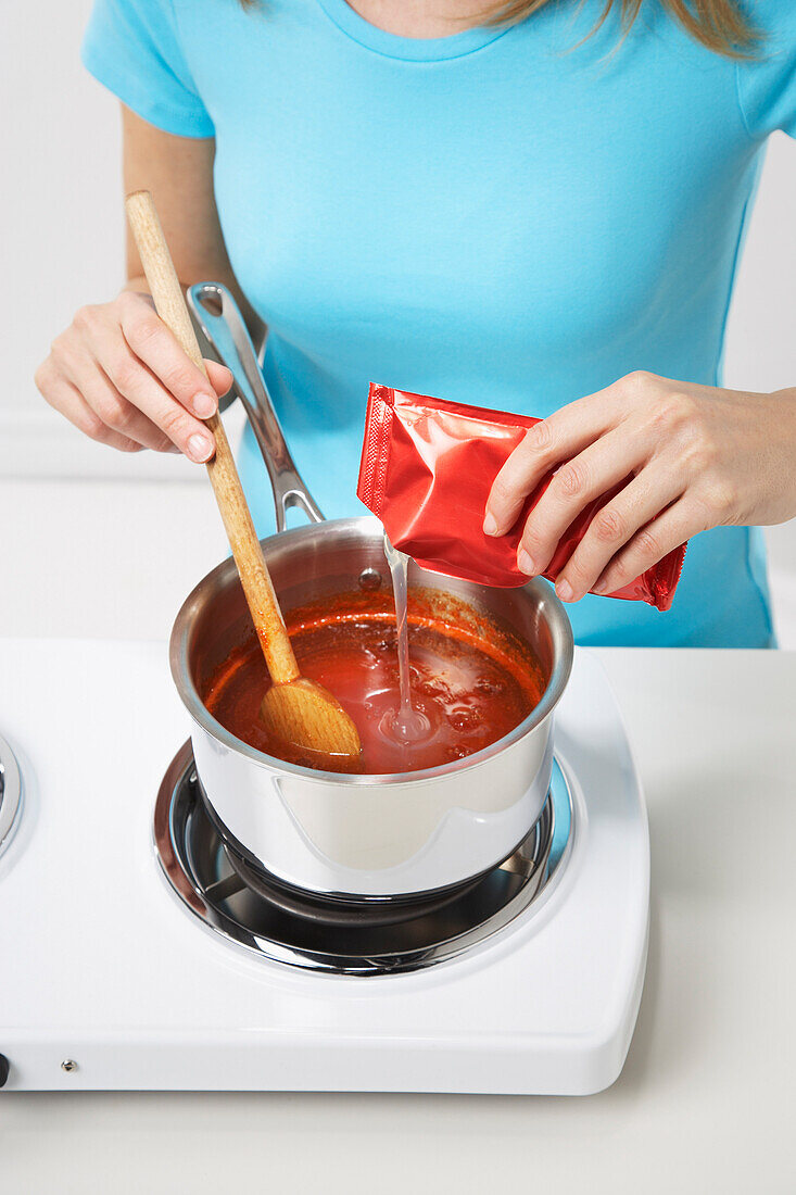 Woman Adding Pectin to Red Pepper Sauce to Make Jelly