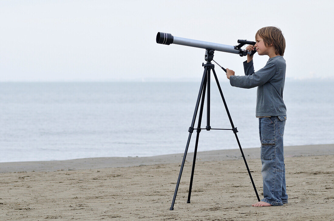 Junge am Strand schaut durch ein Teleskop