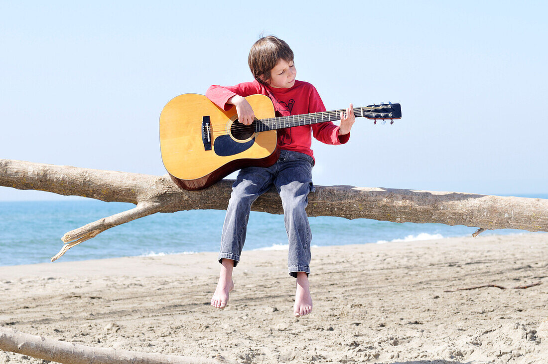 Kleiner Junge spielt Gitarre am Strand