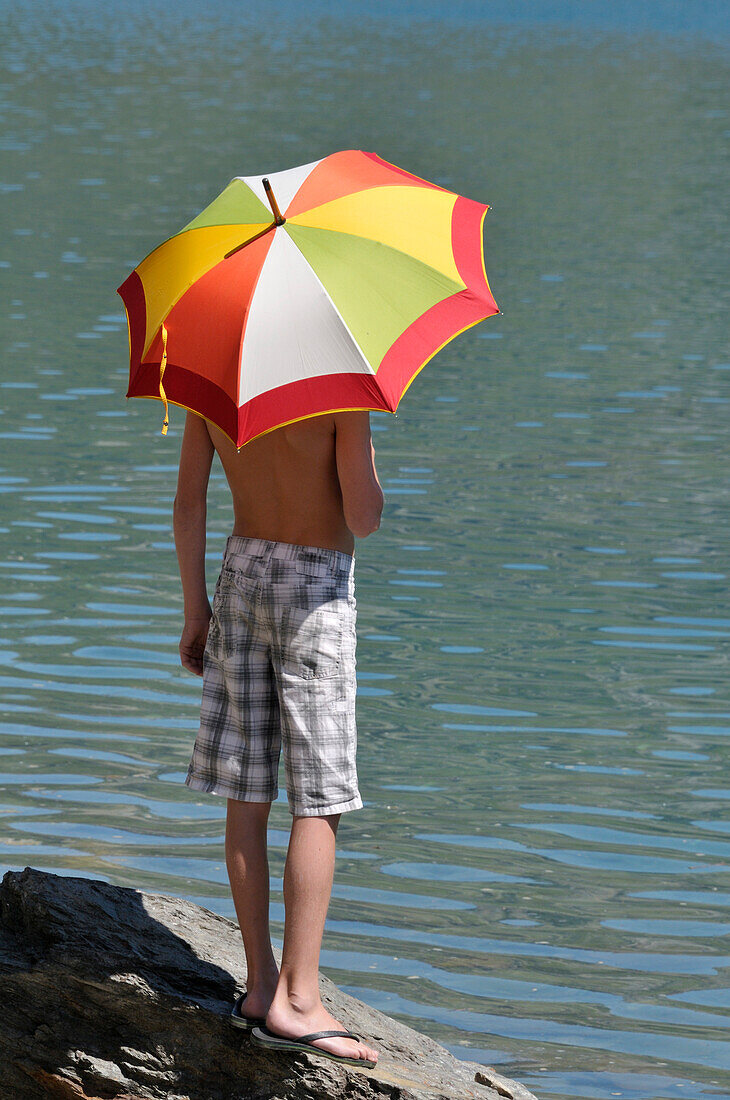 Rückenansicht eines Jungen mit Regenschirm in der Sonne,Alpen,Frankreich