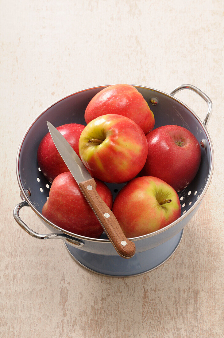 Overhead View of Colander filled with Red Apples and a Knife on Beige Background,Studio Shot