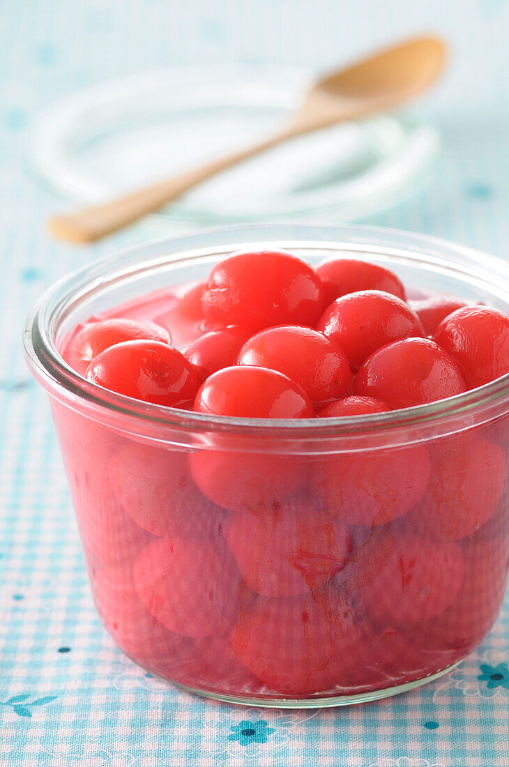 Close-up of Bowl of Cherries in Syrup with Wooden Spoon and Lid in Background