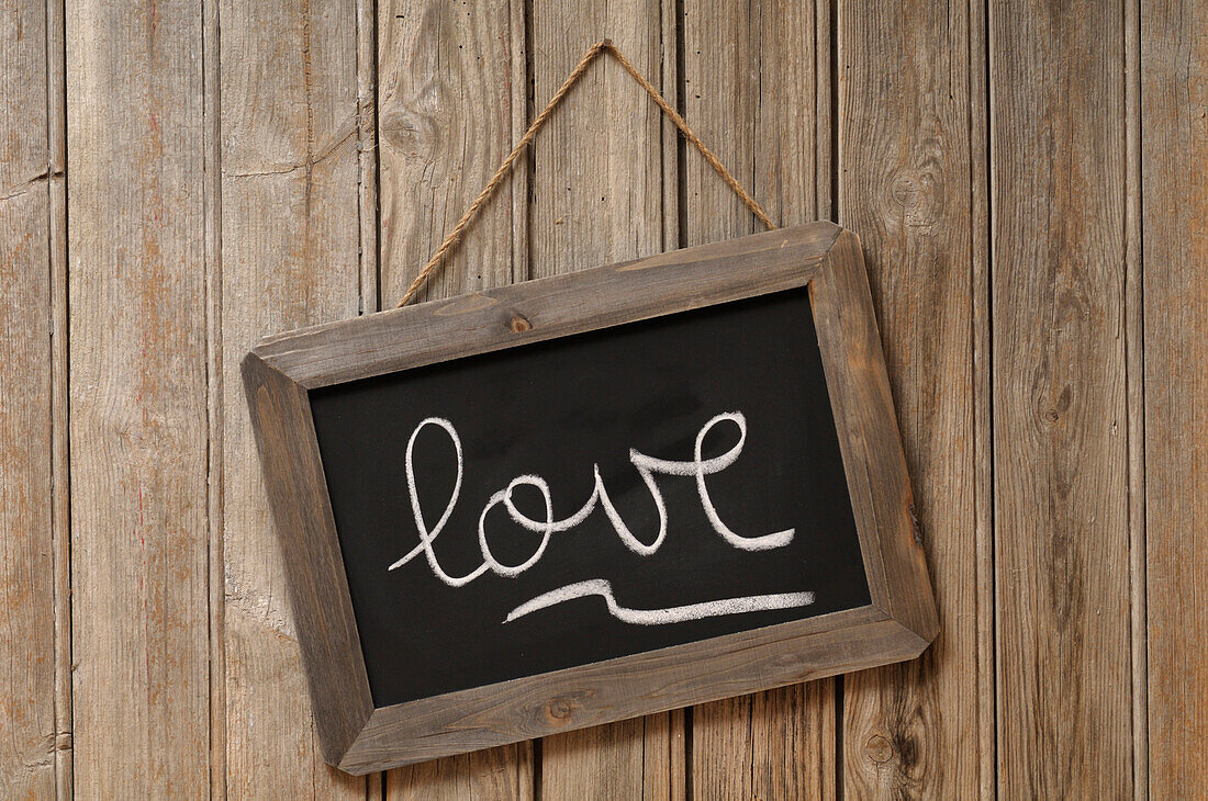 Liebe in Kursivschrift auf Kreidetafel geschrieben und an Holzwand aufgehängt