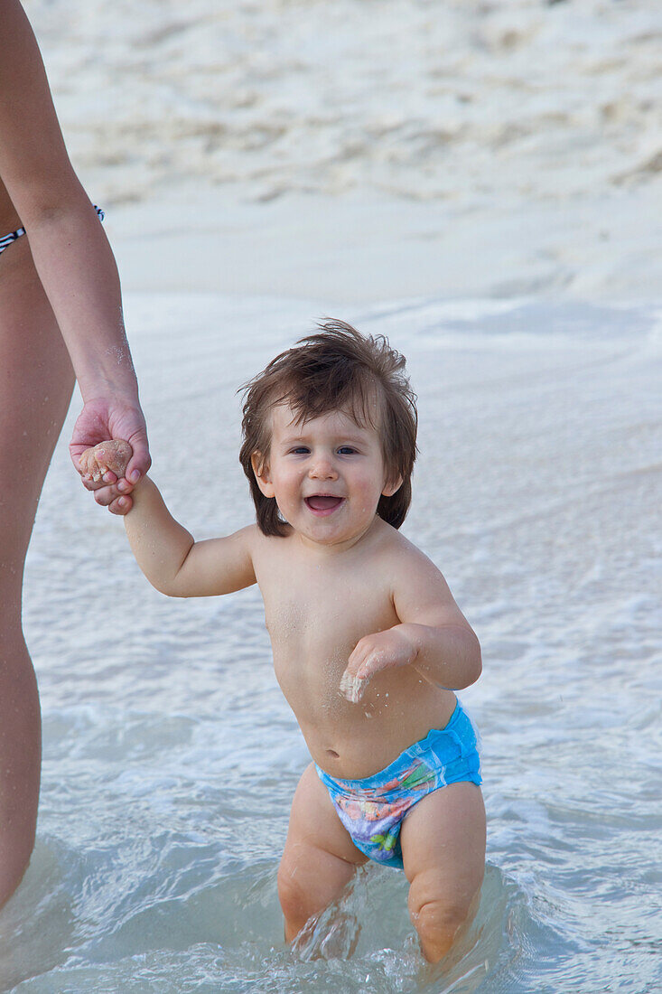 Junge hält die Hand seiner Mutter im Wasser am Strand, Mexiko