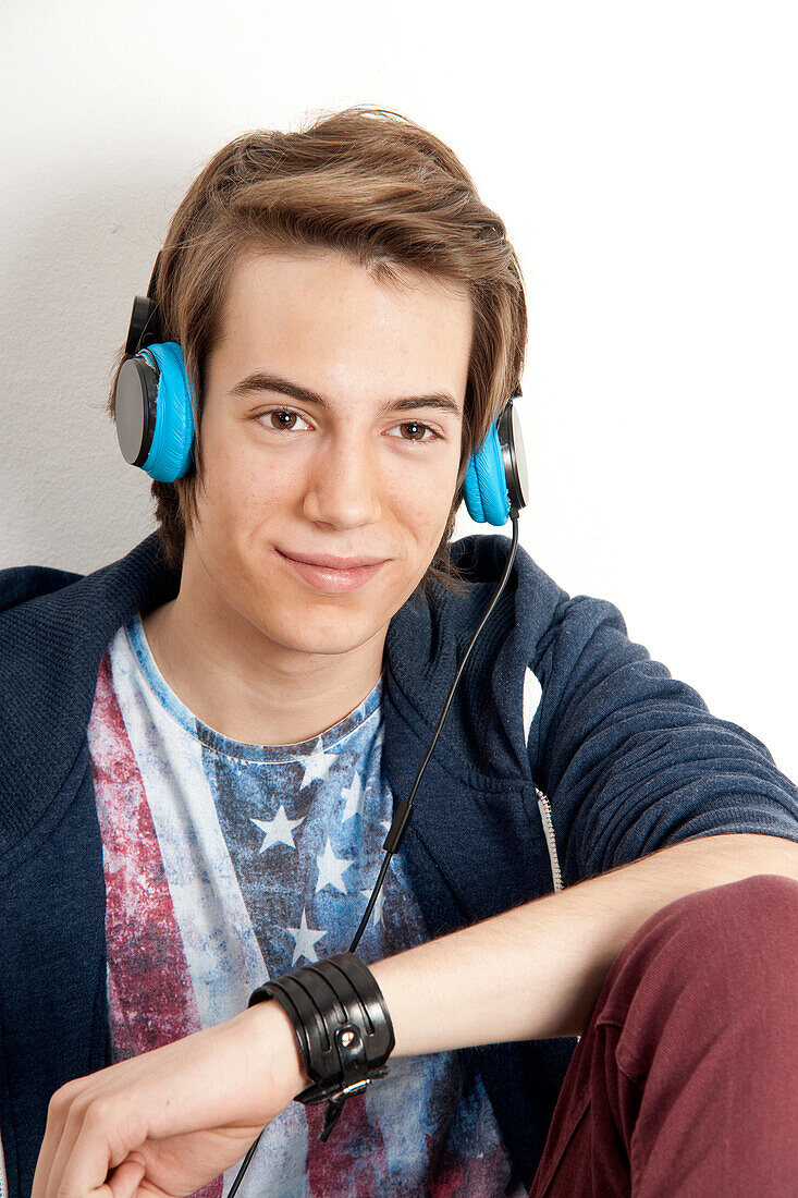 Close-up portrait of teenage boy wearing headphones,listening to music and smiling,studio shot on white background