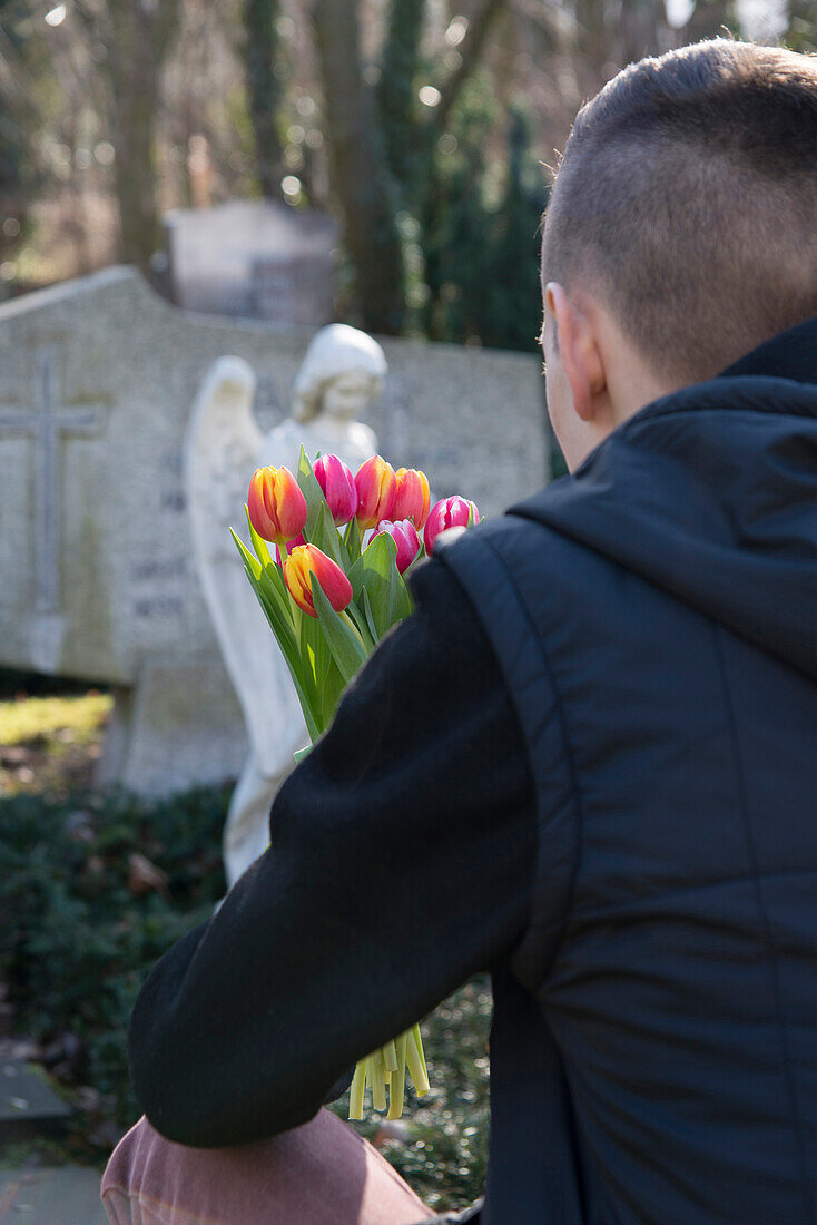 Teenager vor Grabsteinen mit Tulpen auf dem Friedhof