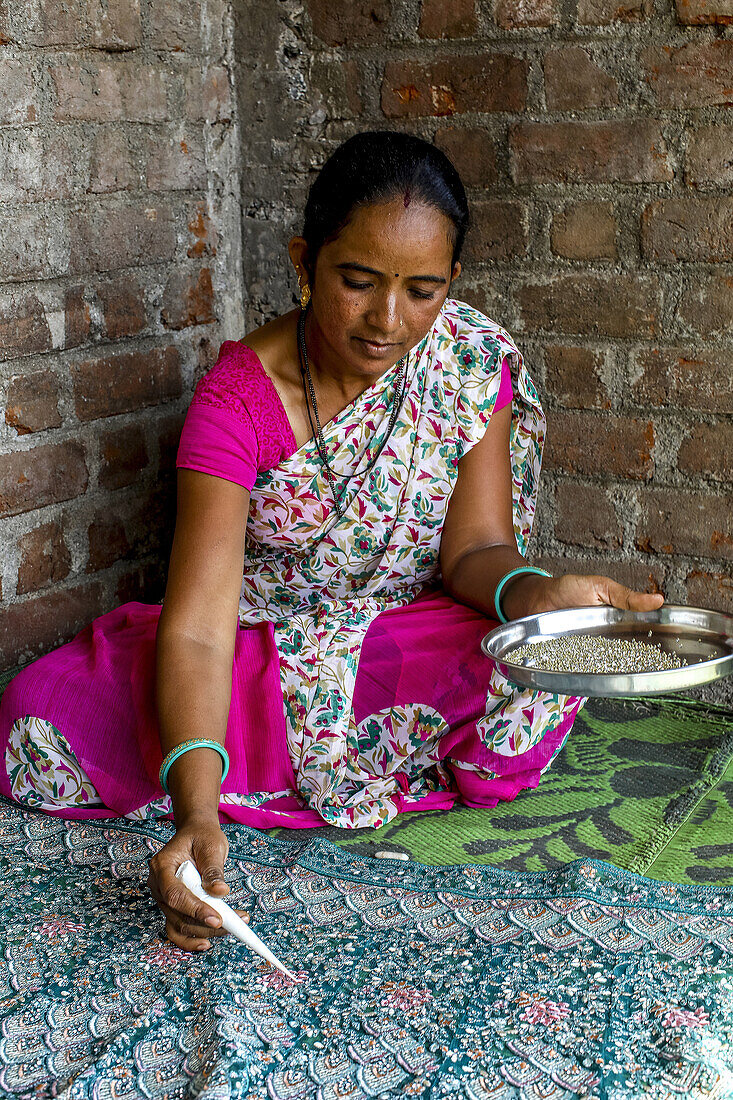 Adivasi woman sticking beads onto a sari in a village in Narmada district,Gujarat,India,Asia