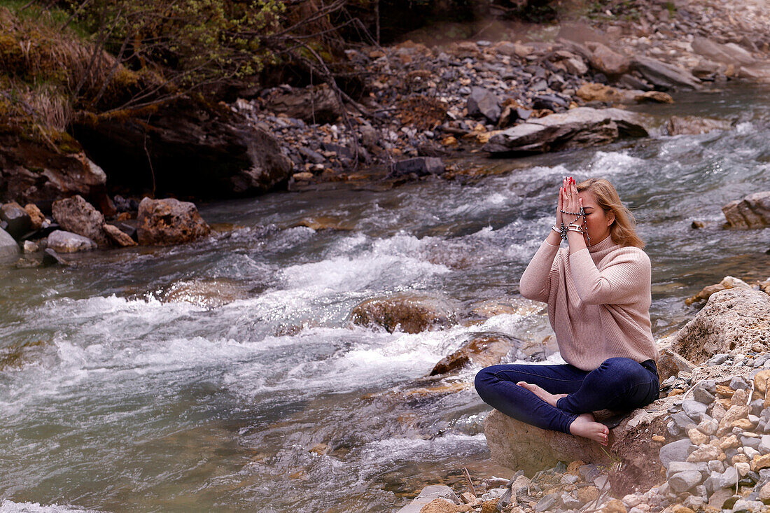 Betende Frau, die auf einem Felsen am Rande eines Flusses sitzt, Konzept der Religion in der Natur, Les Contamines, Haute-Savoie, Frankreich, Europa