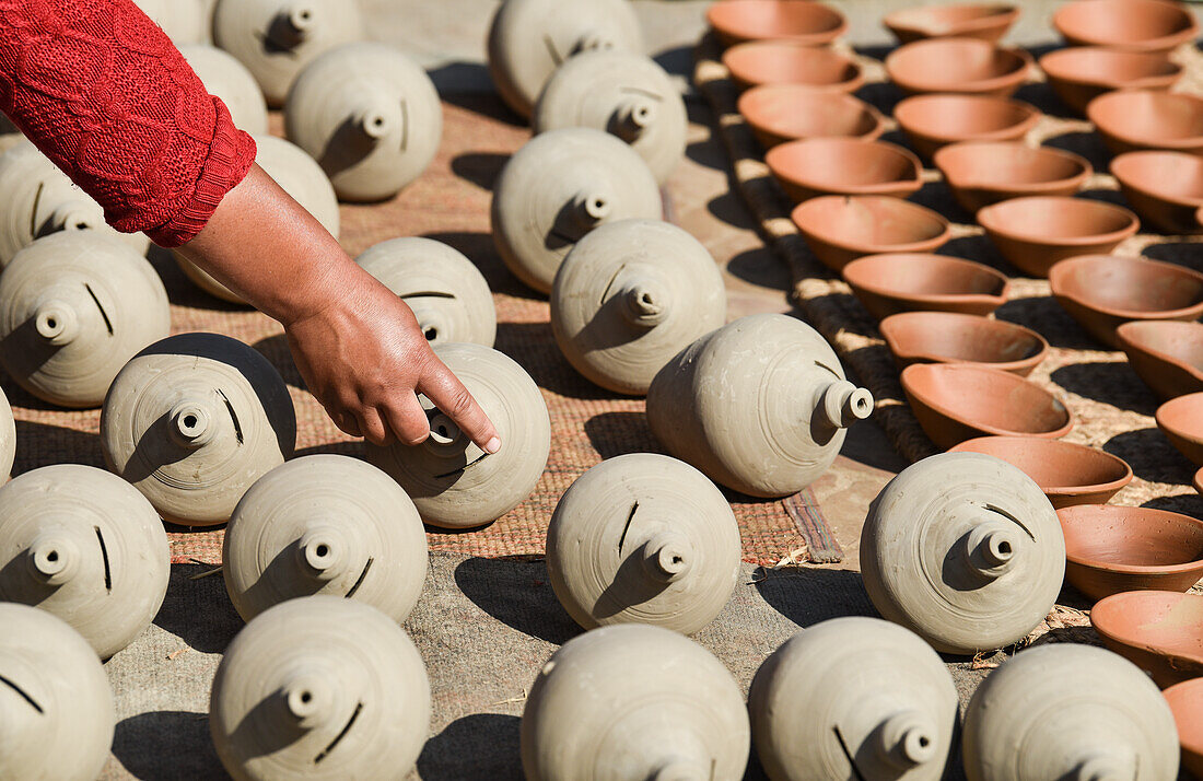 Eine Kunsthandwerkerin zeigt die traditionellen Tontöpfe, die sie in der Sonne trocknen ließ, Bhaktapur, Nepal, Asien