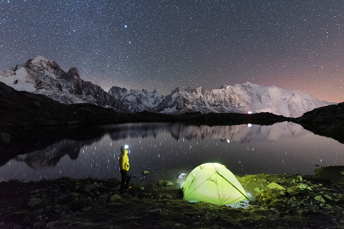 Person bewundert den Sternenhimmel vor dem Zelt am Ufer des Cheserys-Sees, umgeben von der alpinen Landschaft des Mont Blanc, Chamonix, Haute Savoie, französische Alpen, Frankreich, Europa