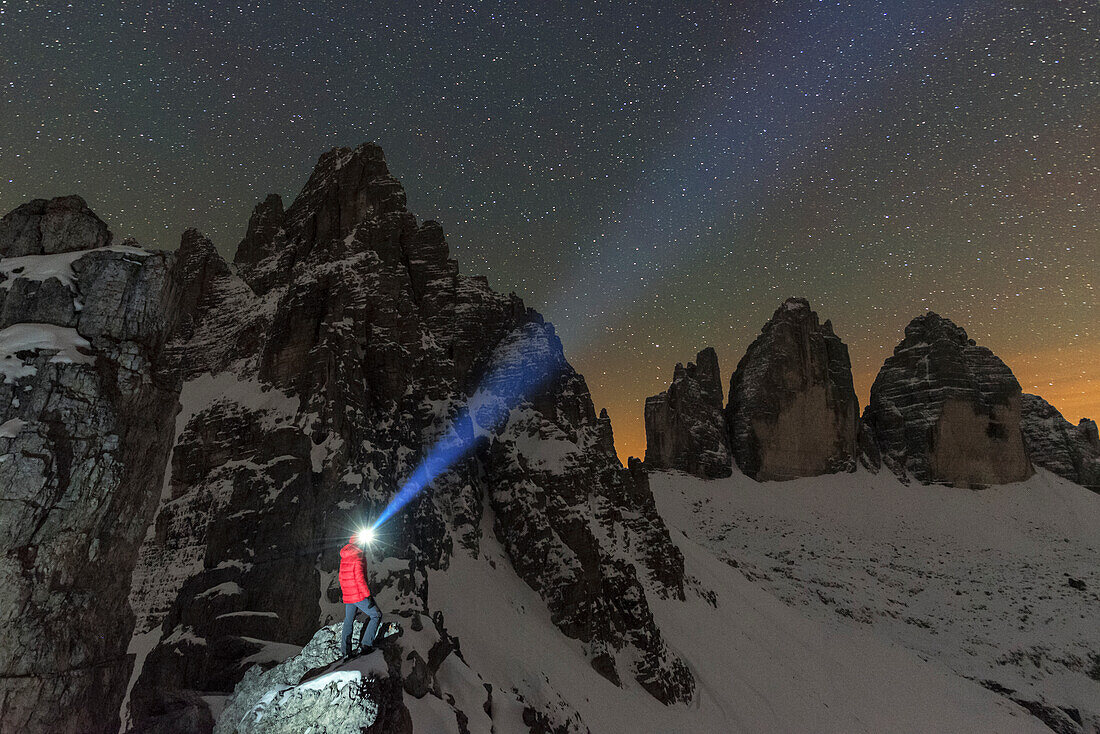 Mann mit Stirnlampe beleuchtet den Sternenhimmel über dem verschneiten Paterno und den Lavaredo-Zinnen, Sexten, Dolomiten, Südtirol, Italien, Europa