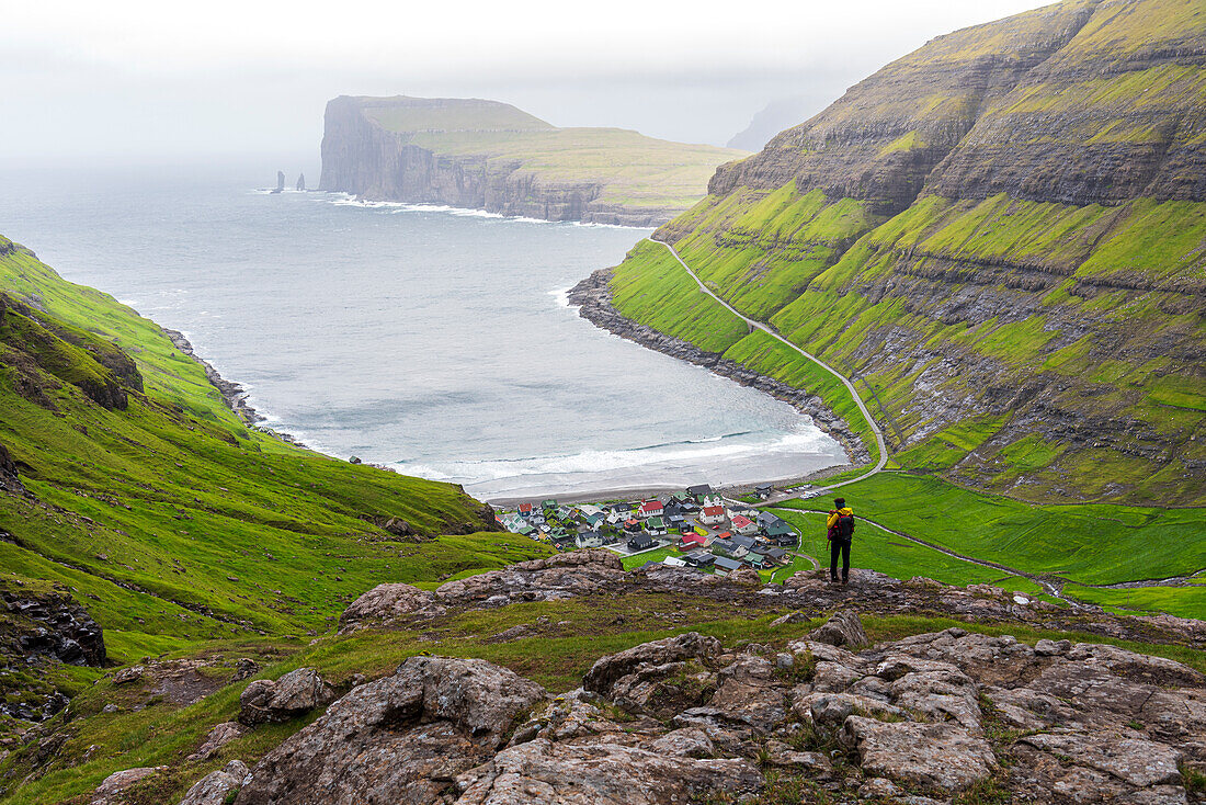 One man on top of a rock admiring the village of Tjornuvik in the misty weather,Sunda municipality,Streymoy island,Faroe islands,Denmark,Europe