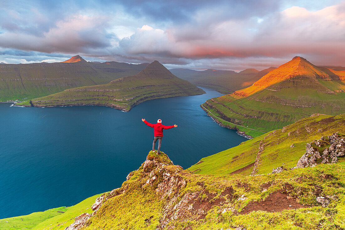 Glücklicher Wanderer steht oben auf der Klippe mit Blick auf den Fjord von Funningur, Insel Eysturoy, Färöer-Inseln, Dänemark, Europa