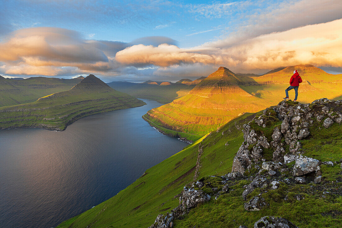 Summer view of a hiker standing on top of a mountain overlooking the fjord at sunrise,Funningur fjord,Eysturoy island,Faroe islands,Denmark,Europe