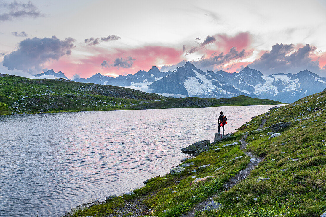 Wanderer steht in der Nähe des Ufers des Fenetre-Sees und bewundert den Sonnenuntergang über dem Massiv des Mont Blanc, Ferret-Tal, Kanton Wallis, Col du Grand-Saint-Bernard (St. Bernhard-Pass), Schweiz, Europa