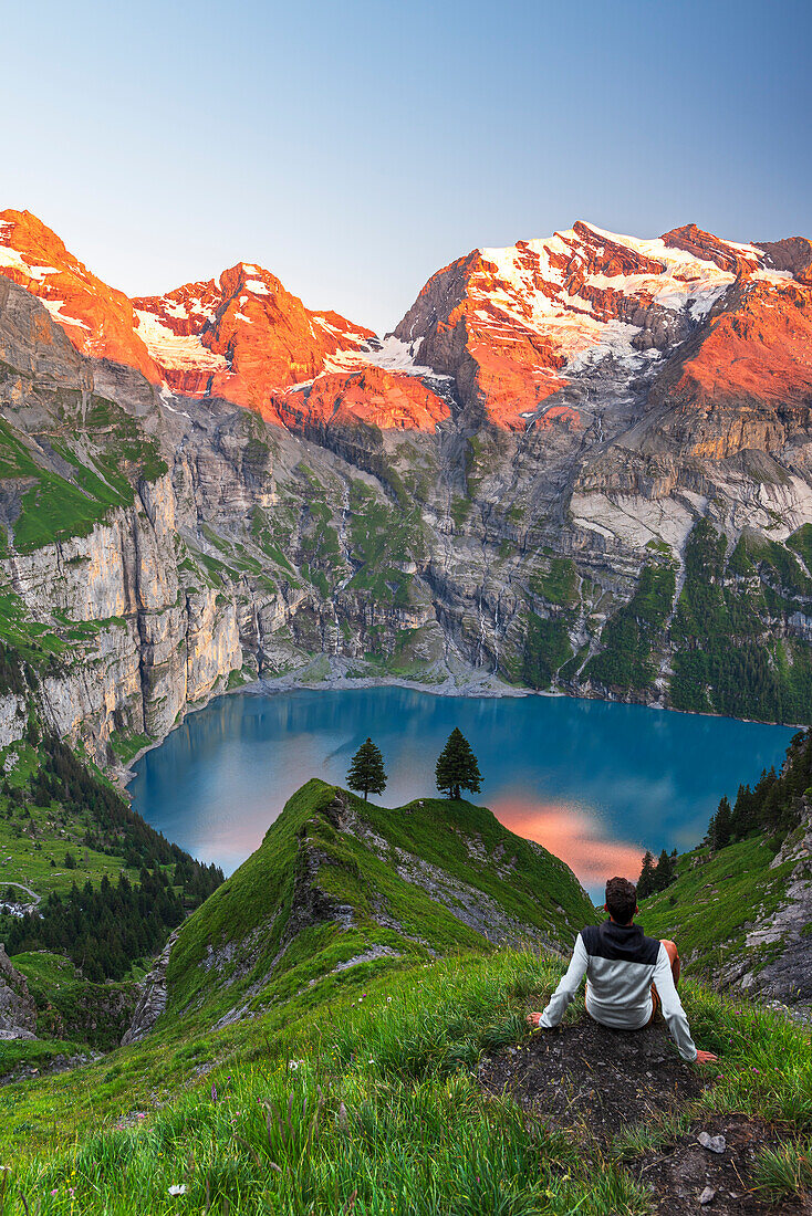 Blick auf einen Wanderer, der vor dem Oeschinensee rastet, umgeben von schneebedeckten Gipfeln bei Sonnenuntergang, Oeschinensee, Kandersteg, Kanton Bern, Schweiz, Europa