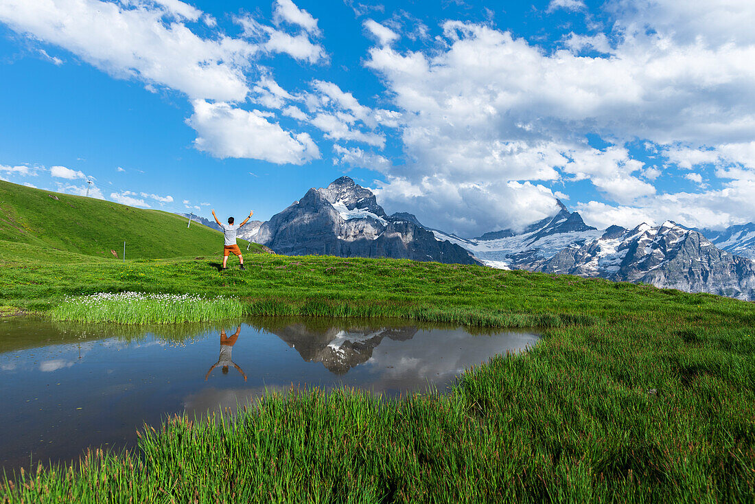 Fröhlicher Wanderer spiegelt sich im Wasser eines kleinen Sees unterhalb der Berner Oberländer Berge, Bachalpsee, Grindelwald, Kanton Bern, Schweiz, Europa
