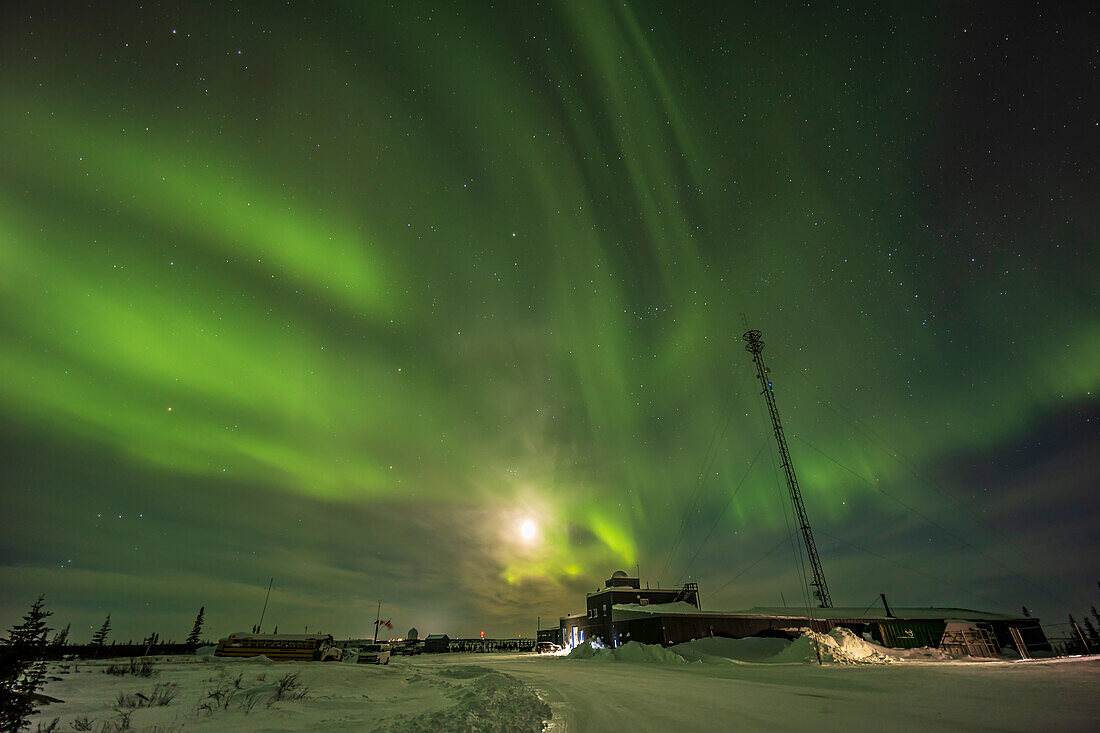 Auroral curtains in the west,with the waxing crescent Moon setting at centre,plus Cassiopeia at top right. This was February 25,2023 from the parking lot at the Churchill Northern Studies Centre,Churchill,Manitoba. The old Rocket Range headquarters building is at right.
