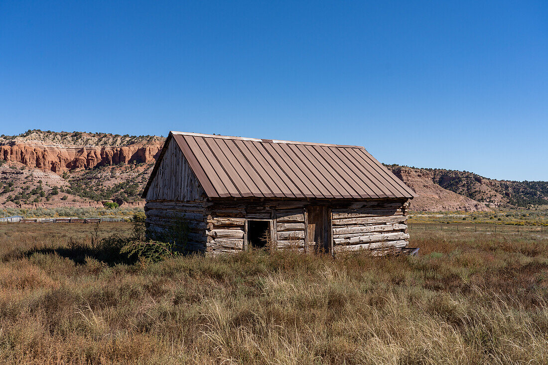An old log cabin on a ranch near Cannonville in southwest Utah with eroded sandstone cliffs behind.