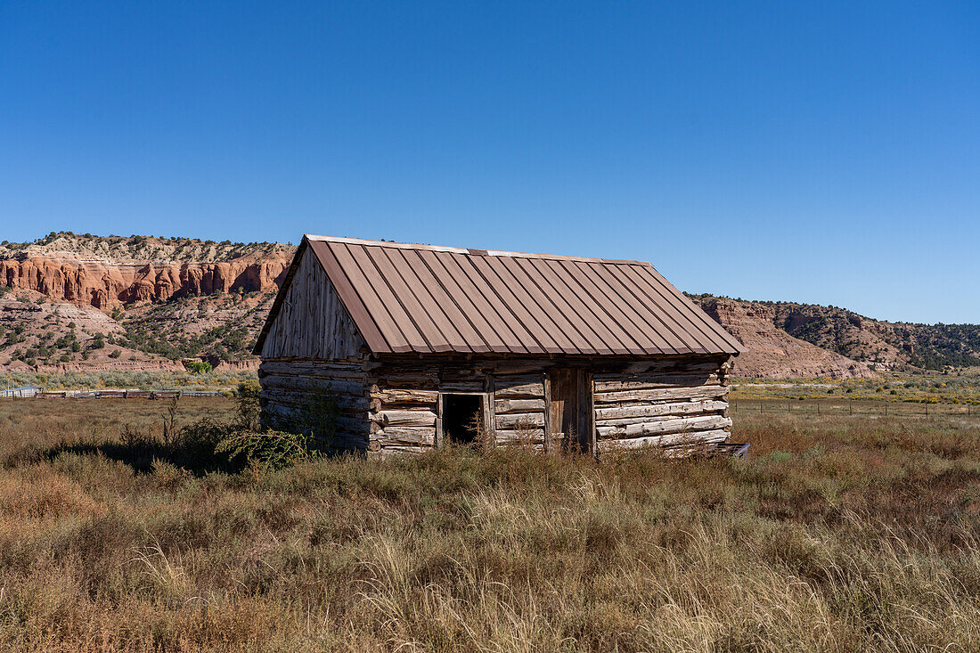 Eine alte Blockhütte auf einer Ranch in der Nähe von Cannonville im Südwesten Utahs mit erodierten Sandsteinklippen im Hintergrund.