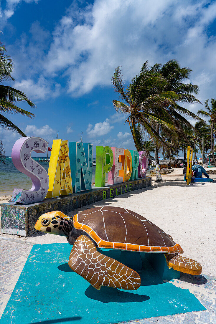 Palmen und eine Meeresschildkrötenstatue vor einem 3-D-Schild am Strand von San Pedro auf Ambergris Caye, Belize.