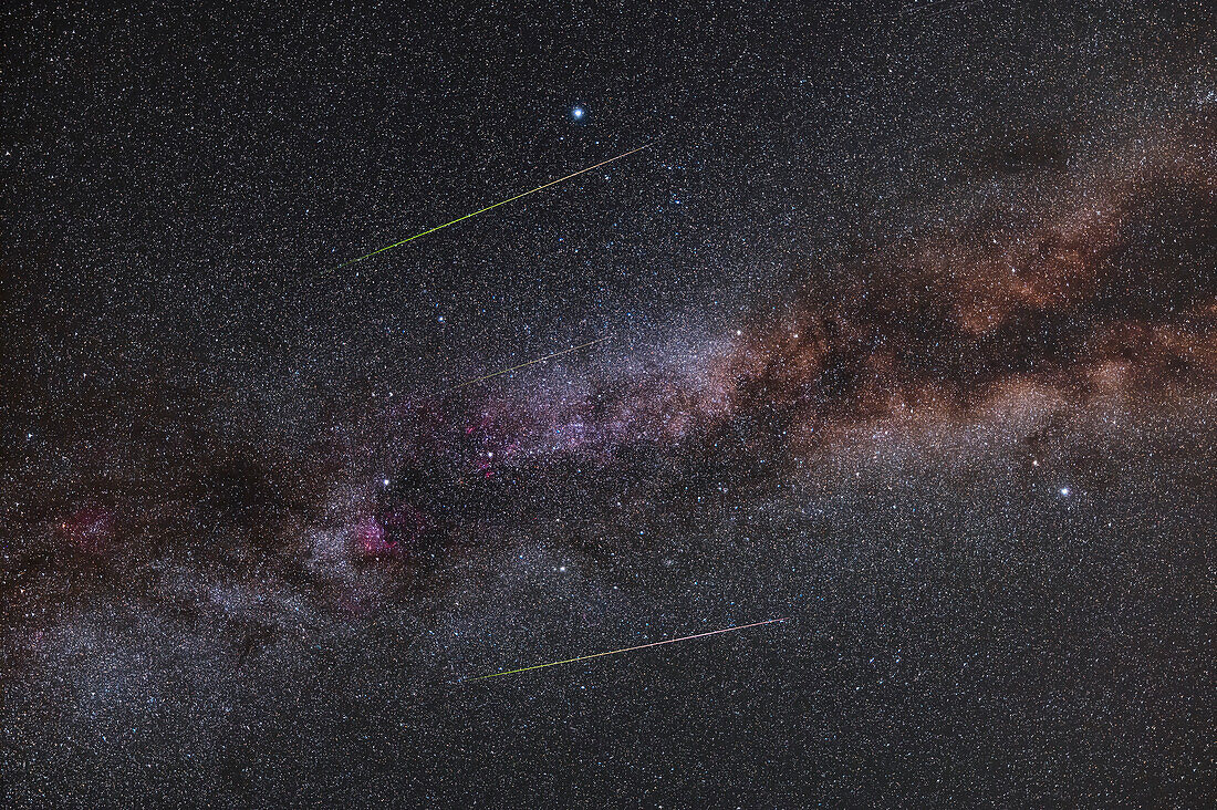 Ein Trio von Perseiden-Meteoren, die von links nach rechts vom Radianten im Perseus (links außerhalb des Bildes) über die Sommermilchstraße im Schwan und in der Leier ziehen. Die Meteore zeigen den charakteristischen Übergang von Grün zu Rot entlang ihrer Ionisationsbahn. Im Bildausschnitt sind die Sterne des Sommerdreiecks, Deneb, Wega und Altair zu sehen.