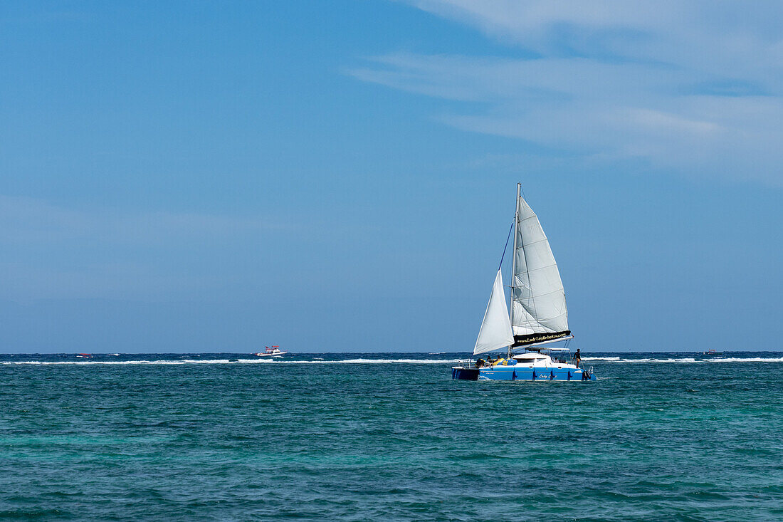 A catamaran sailboat on a sailing tour in the Caribbean Sea at San Pedro on Ambergris Caye in Belize. The wave break at the Belize Barrier Reef is visible behind with a dive boat outside the reef.