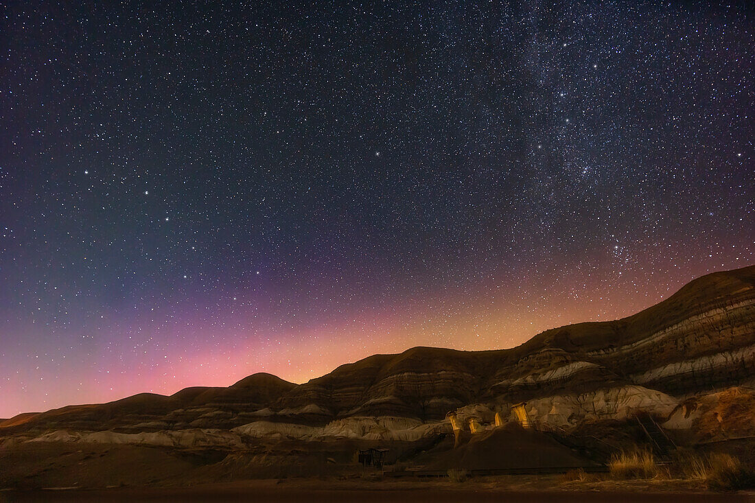 Der nördliche Himmel über den Hoodoos Badlands im Tal des Red Deer River in der Nähe von Drumheller, Alberta, in einer Nacht, in der einige Polarlichter den Himmel gelb und magenta färben, mit einem Hauch von Blau. Der Vordergrund wird teilweise von einer Hofbeleuchtung in der Nähe und von Autoscheinwerfern beleuchtet. Der Große Wagen ist links, der Polarstern und der Kleine Wagen sind über der Mitte, das W der Kassiopeia ist rechts oben.