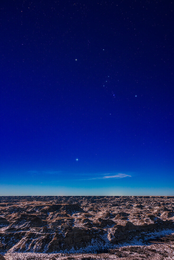 Orion und Sirius über den mondbeschienenen Badlands des Dinosaur Provincial Park, Alberta, am 4. Februar 2023, wobei der zunehmende Gibbous-Mond in dieser sehr klaren und milden Nacht für die Beleuchtung sorgt.