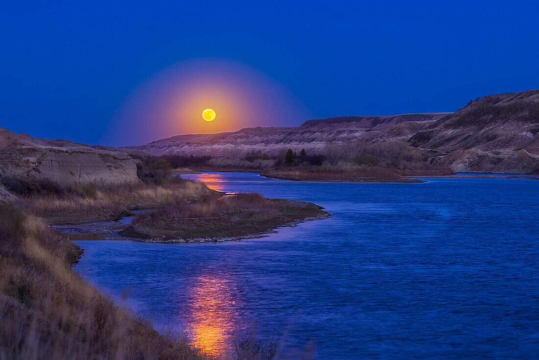 The rising Full Moon of May 5,2023,coming up over the Red Deer River near East Coulee,Alberta. The Moon is illuminating the water with a fine golden glitter path.