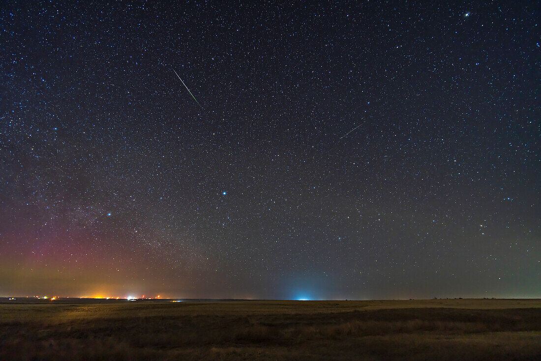 Two lone Lyrid meteors on the peak of the meteor shower night,April 22,2023. Two captured out of 342 frames taken over 2 hours. The sky and ground come from the exposure with the bright meteor on it,when a dim aurora was also on the northeast horizon. The bright meteor shows the classic green to pink gradient of colours. Vega and Lyra are rising at lower centre. Deneb and Cygnus are at left. Arcturus is at upper right.