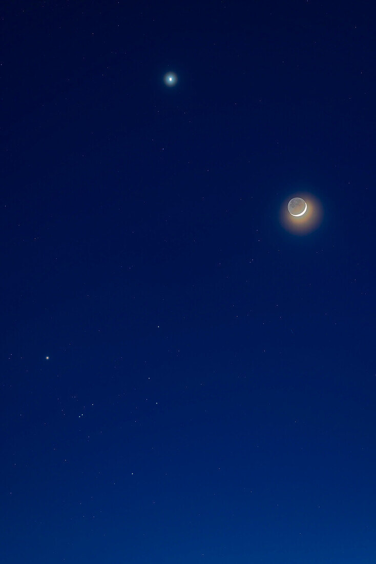 Dies ist die Zusammenkunft der zunehmenden Mondsichel am Abend des 22. April 2023 unterhalb der Venus und in der Nähe des Hyaden-Sternhaufens im Stier. Der schwache Erdschein ist auf der dunklen Seite des Mondes sichtbar. Hohe Wolken haben das natürliche Leuchten von Mond und Venus verstärkt.
