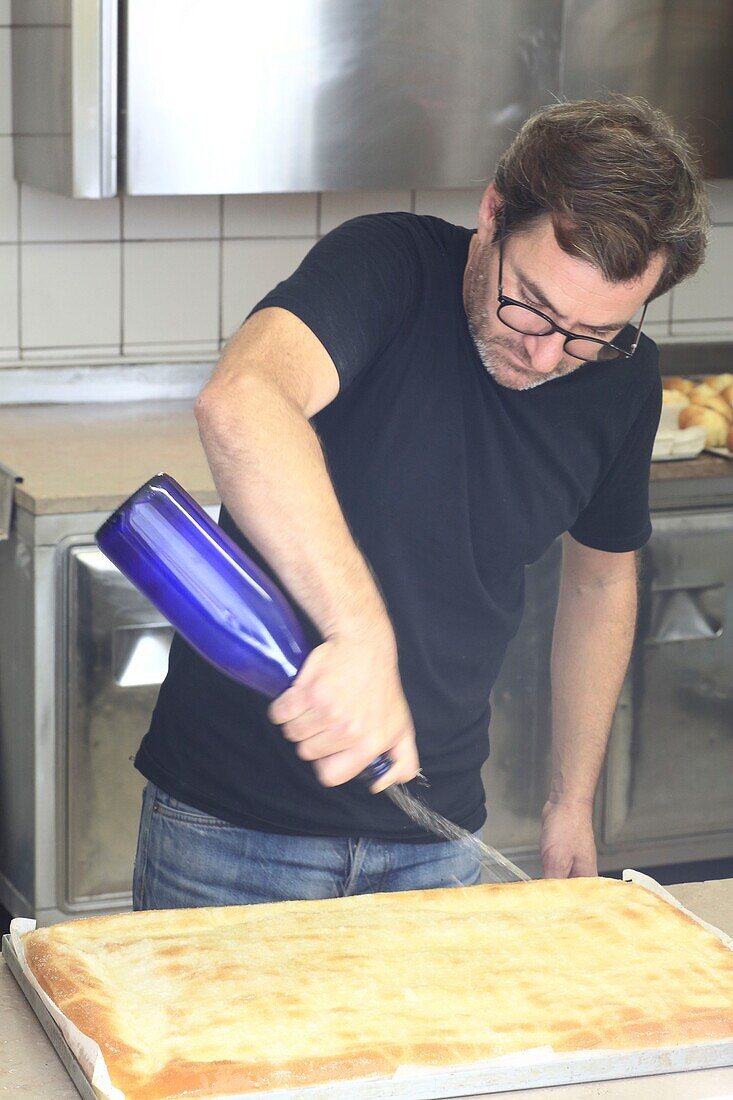 Frankreich, Gard, Petite Camargue, Aigues-Mortes, Bäcker Laurent Poitavin begießt die Zuckerfougasse von Aigues-Mortes mit Orangenblütenwasser